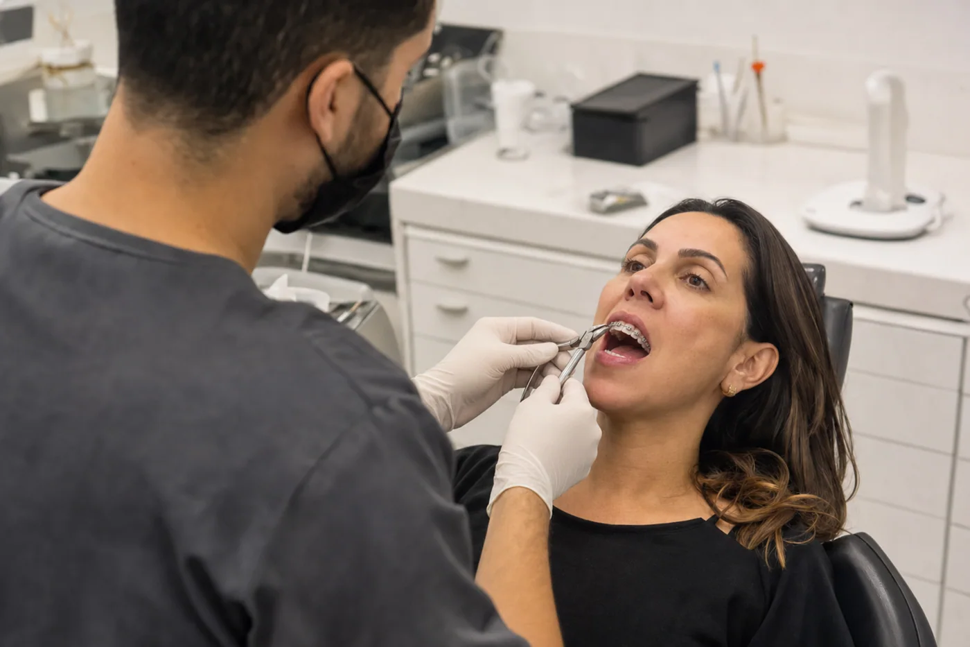 Dr. Franklin Araújo de costas ajustando aparelho ortodôntico fixo em paciente adulta no consultório da Sobilis — Itapoã, Belo Horizonte